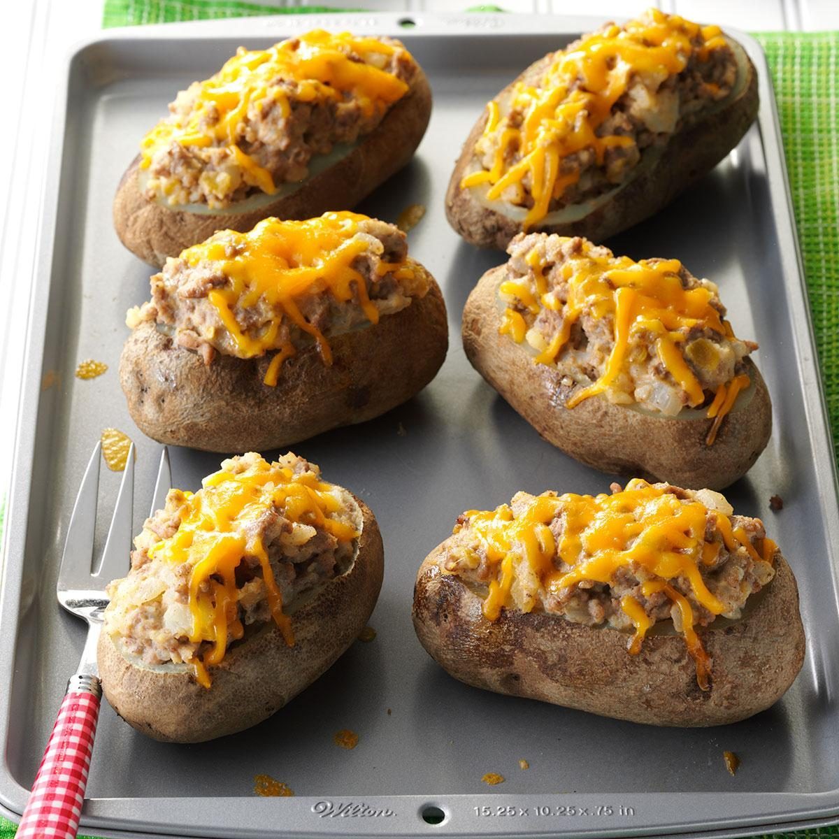 Potatoes topped with melted cheese are baked on a silver tray, placed on a green cloth.