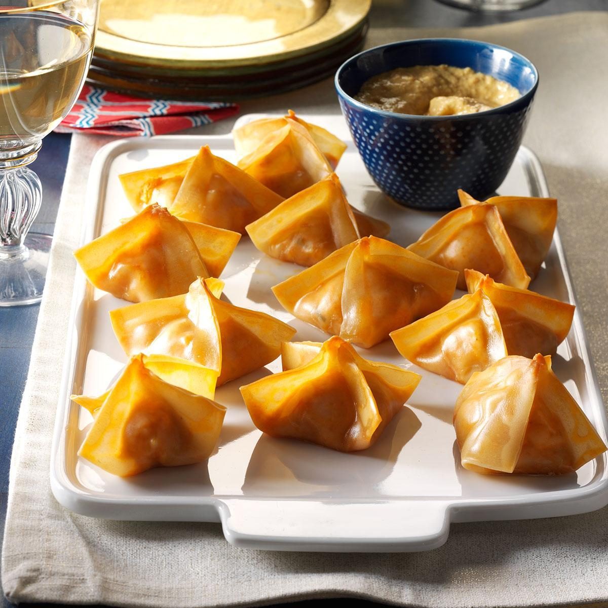 Wontons arranged on a platter, accompanied by a dipping sauce in a small bowl, next to a glass and colorful napkin.