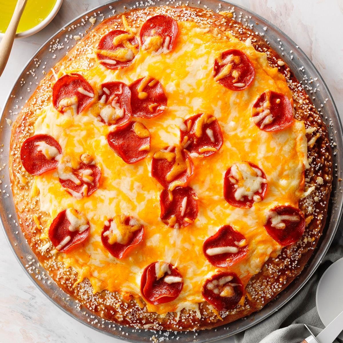 Pizza topped with pepperoni and melted cheese on a metal tray, surrounded by a sprinkle of parmesan, next to a bowl of dipping sauce.