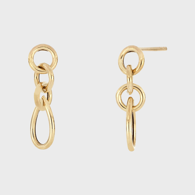 Gold earrings feature interlocking loops, held against a plain white background.