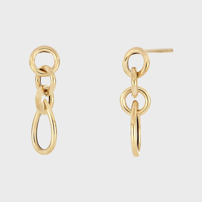 Gold earrings feature interlocking loops, held against a plain white background.
