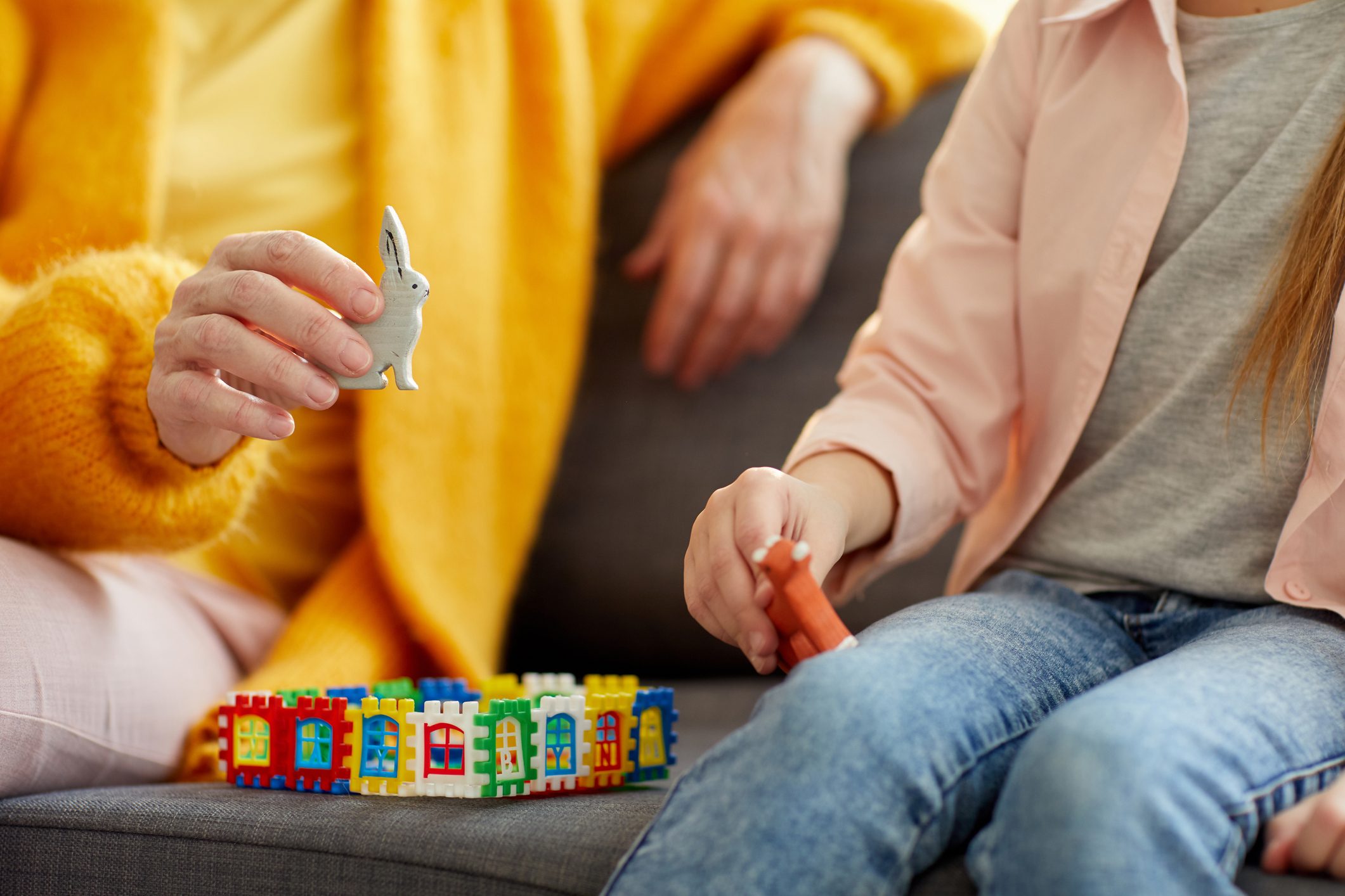 Hands hold toy animals, engaging in imaginative play with colorful building blocks on a couch.