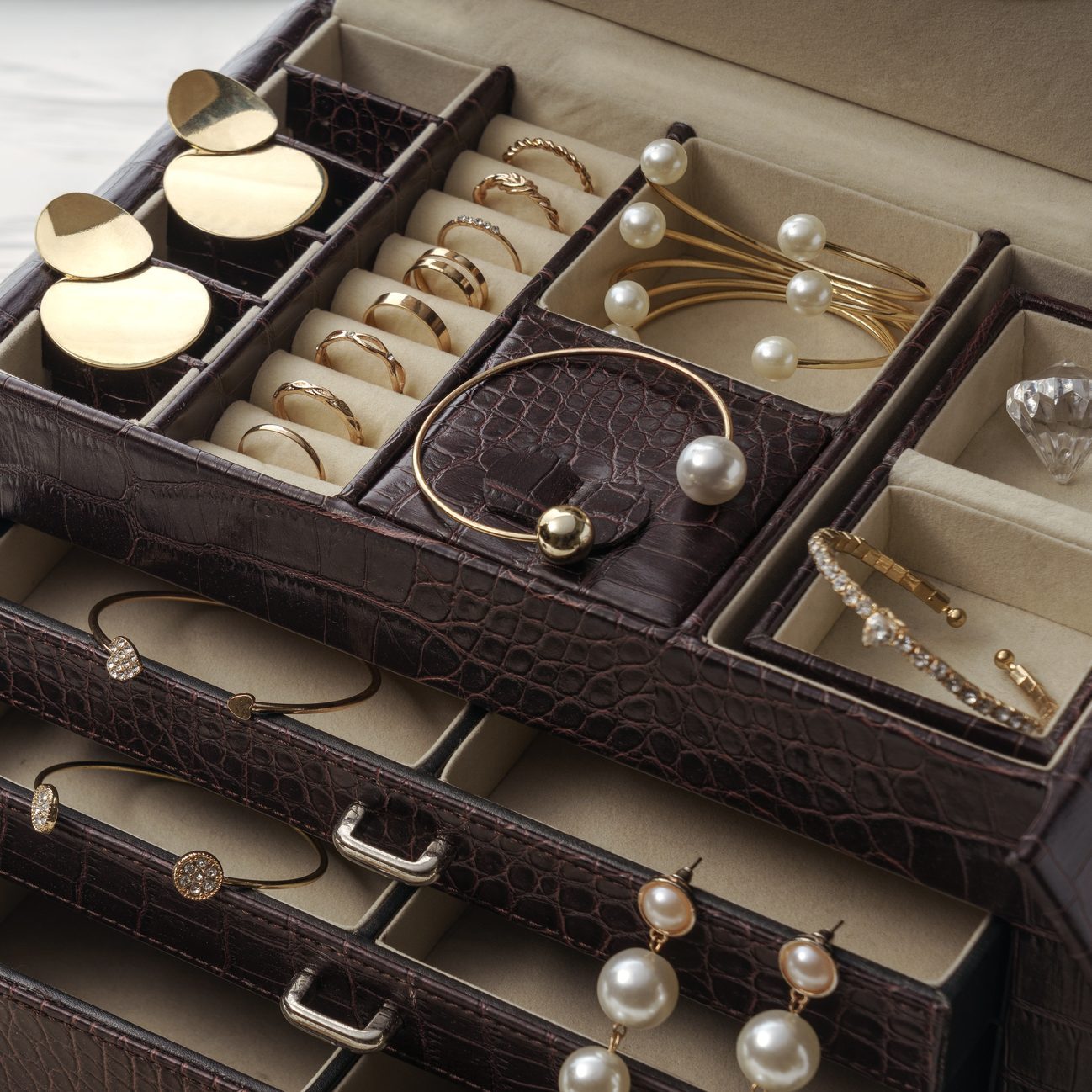 Jewelry rests organized in a leather box, showcasing gold rings, pearl bracelets, and drop earrings in segmented compartments, enhancing elegance and accessibility.
