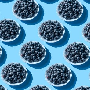 Plates filled with blueberries arranged in a repetitive pattern on a solid light blue background.