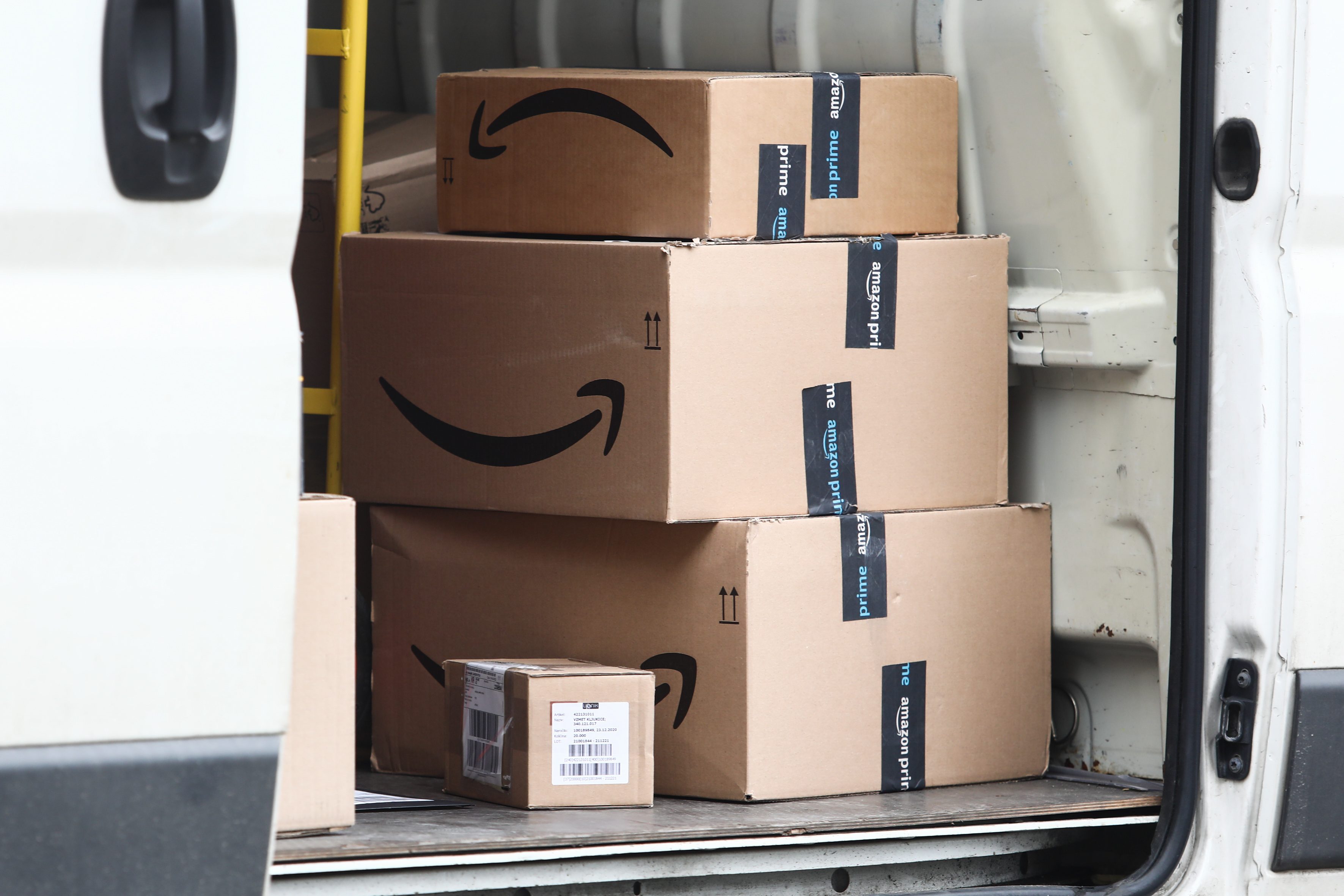 Boxes sit stacked inside a white delivery van, marked with Amazon logos and tape, ready for transport.