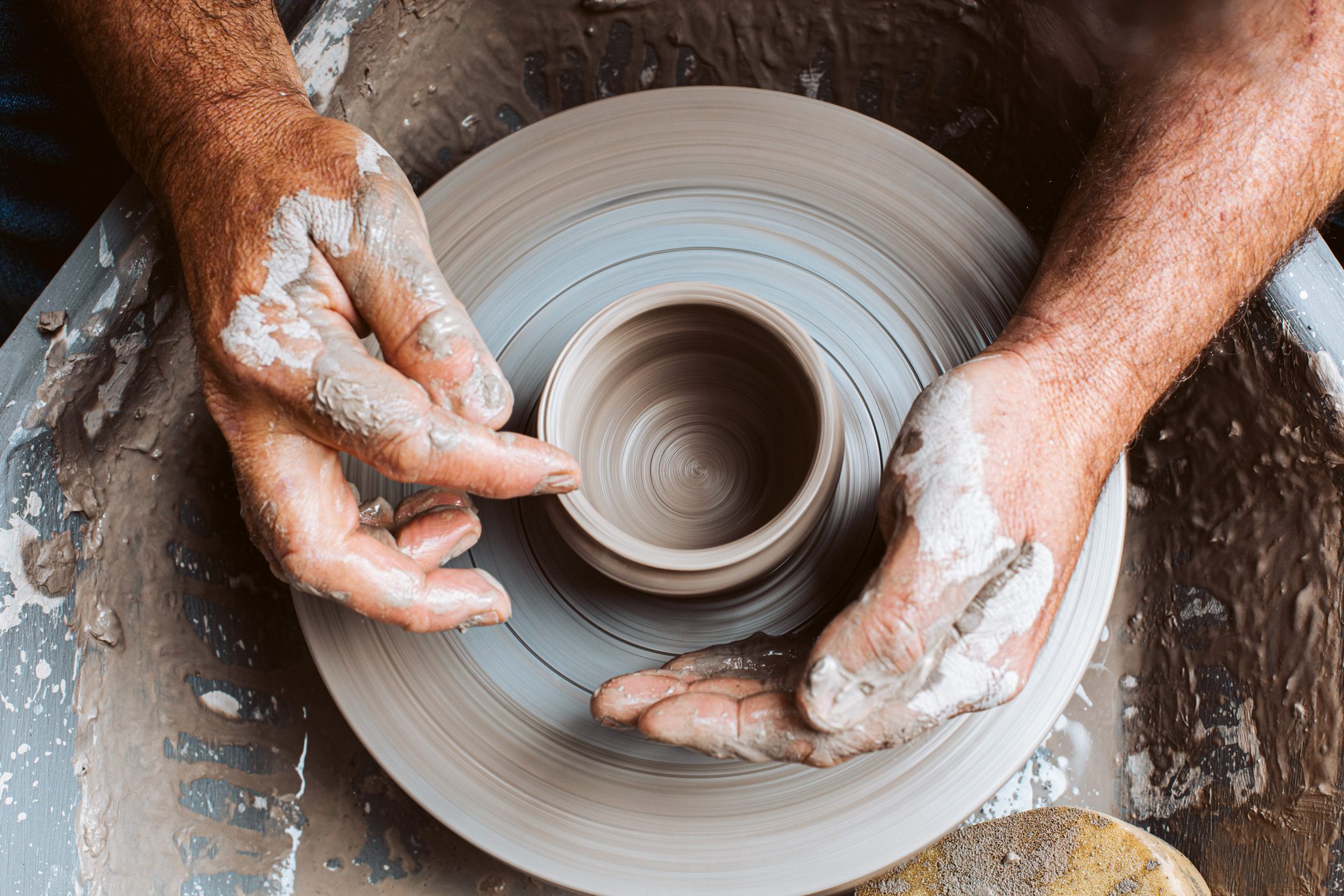 Hands shape clay on a spinning pottery wheel, surrounded by wet clay residue.
