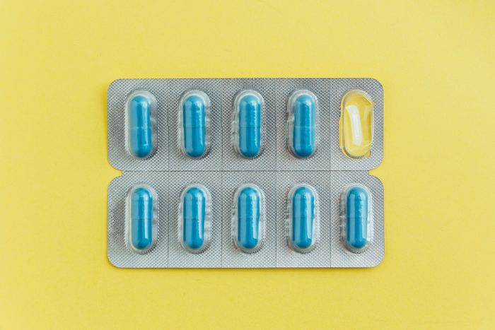 Blister pack of blue capsules with one pill missing on yellow background