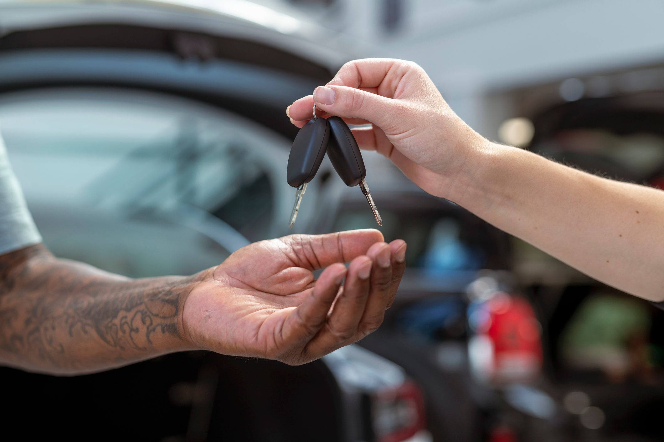 Hands exchange car keys, background showing a blurred open car door.
