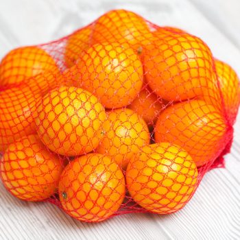 Oranges contained in a red mesh bag lie on a light wooden surface.