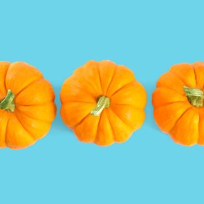 Three small orange pumpkins aligned side by side against a bright blue background.