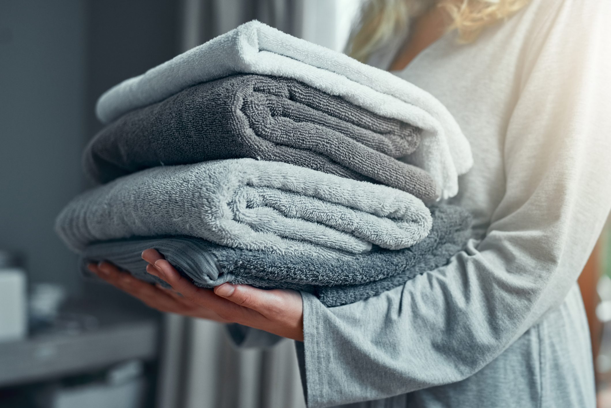 Folded towels rest in a person's arms, held carefully in a softly lit room.