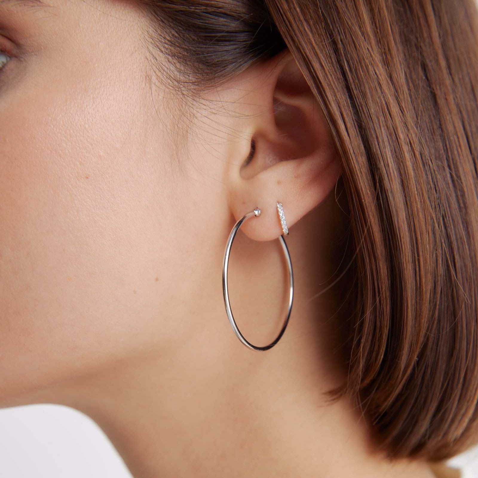 Large hoop earring dangles from a woman's ear, paired with a small stud, against a backdrop of brown hair and skin.