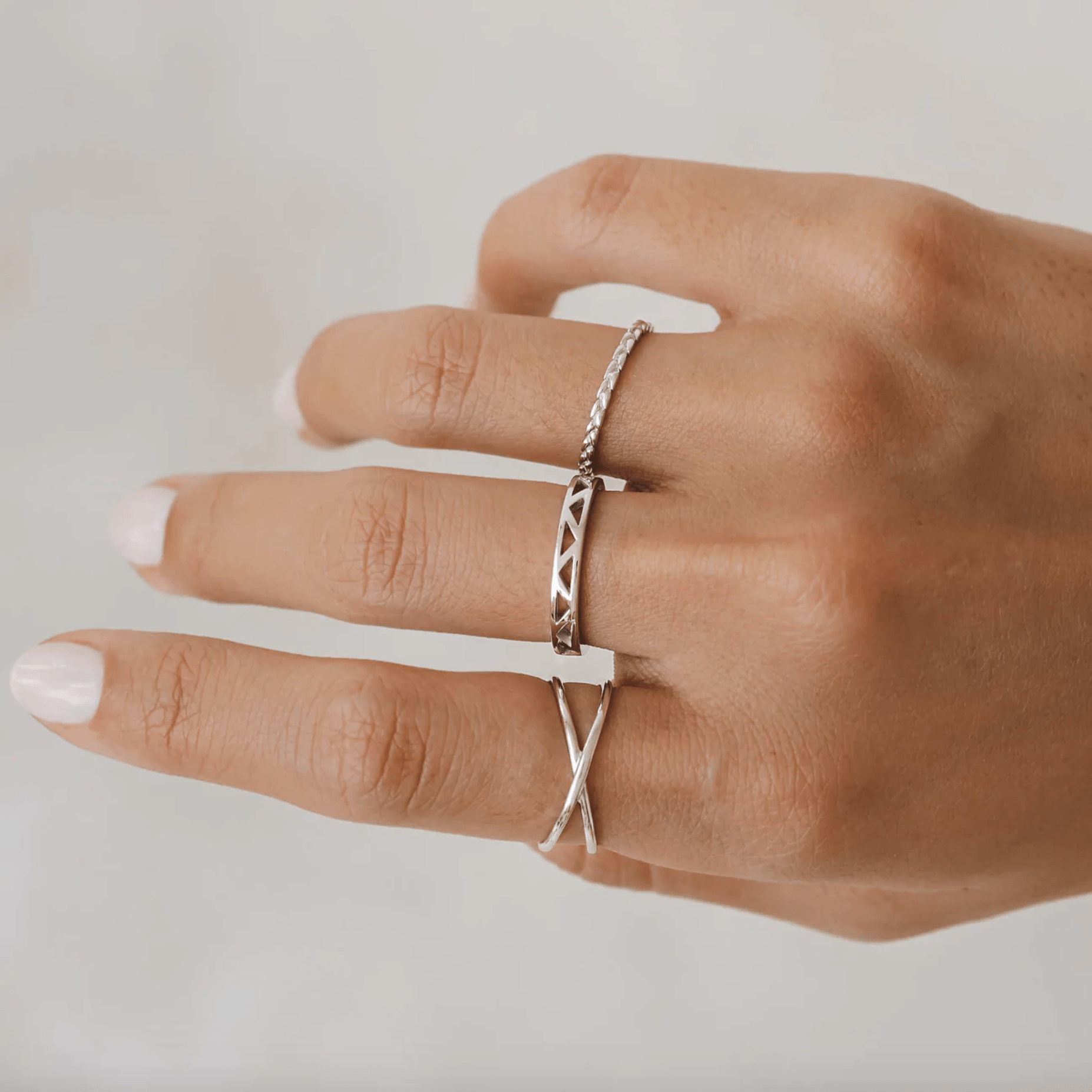 Hand adorned with three silver rings, positioned in a neutral pose against a plain background. The rings feature unique designs and textures.