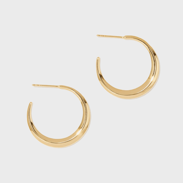 Gold crescent-shaped earrings rest separately on a plain white background, showcasing their smooth, polished design and open-loop form.