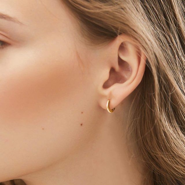 A golden hoop earring is worn, complementing a person's ear against a backdrop of light brown hair.