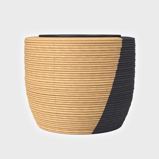A large, round basket woven with alternating tan and black bands sits on a plain white background.