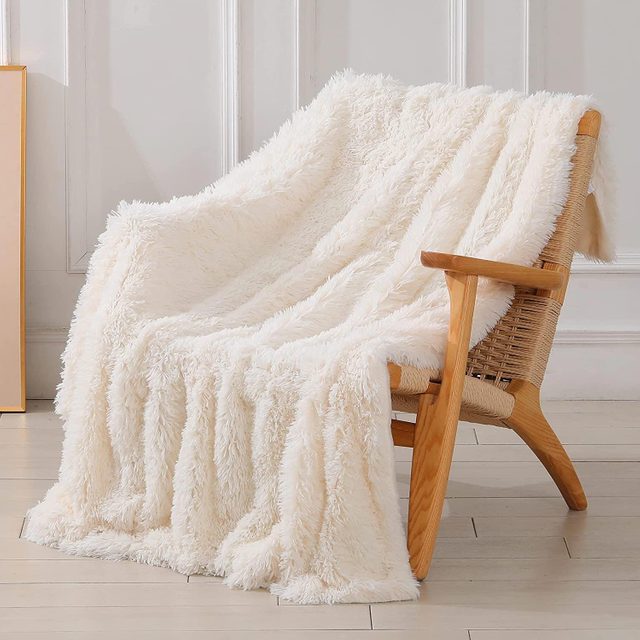 A fluffy white throw drapes over a wooden chair, set against a light-colored, panelled wall in a cozy, well-lit room.