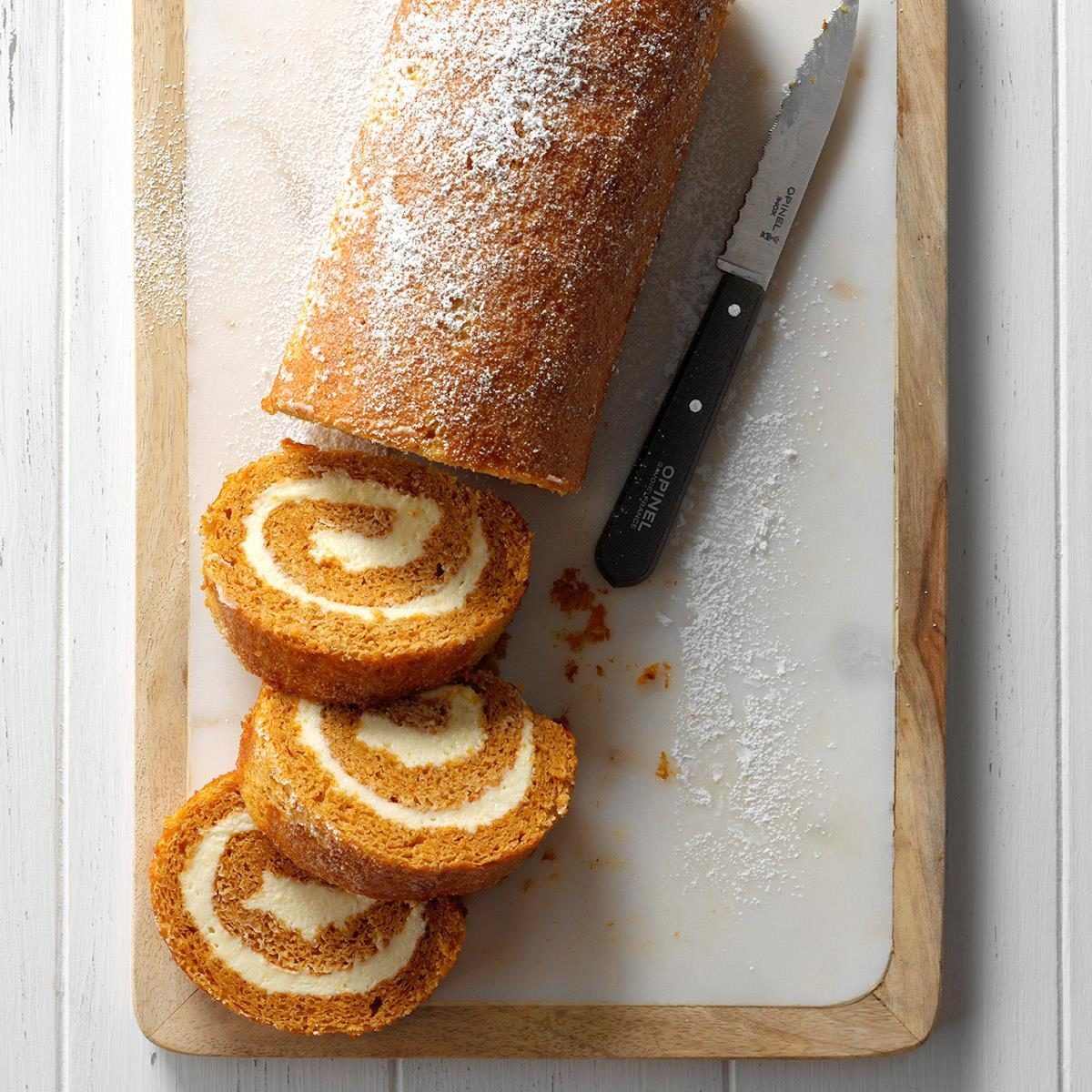 Cake roll is sliced, dusted with powdered sugar on a wooden cutting board, accompanied by a serrated knife.