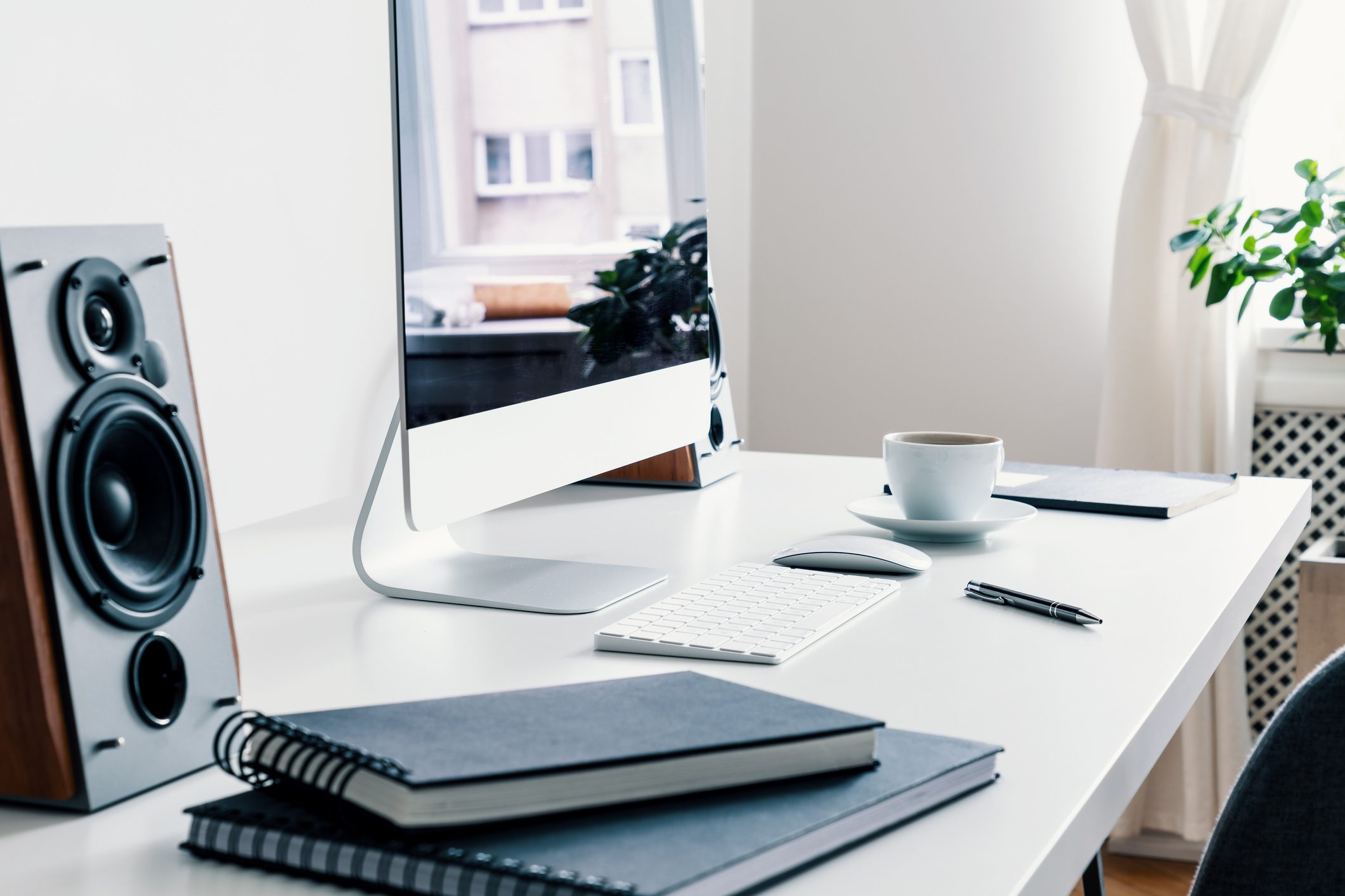 Close-up on books, speaker and desktop computer on desk in white freelancer's interior. Real photo