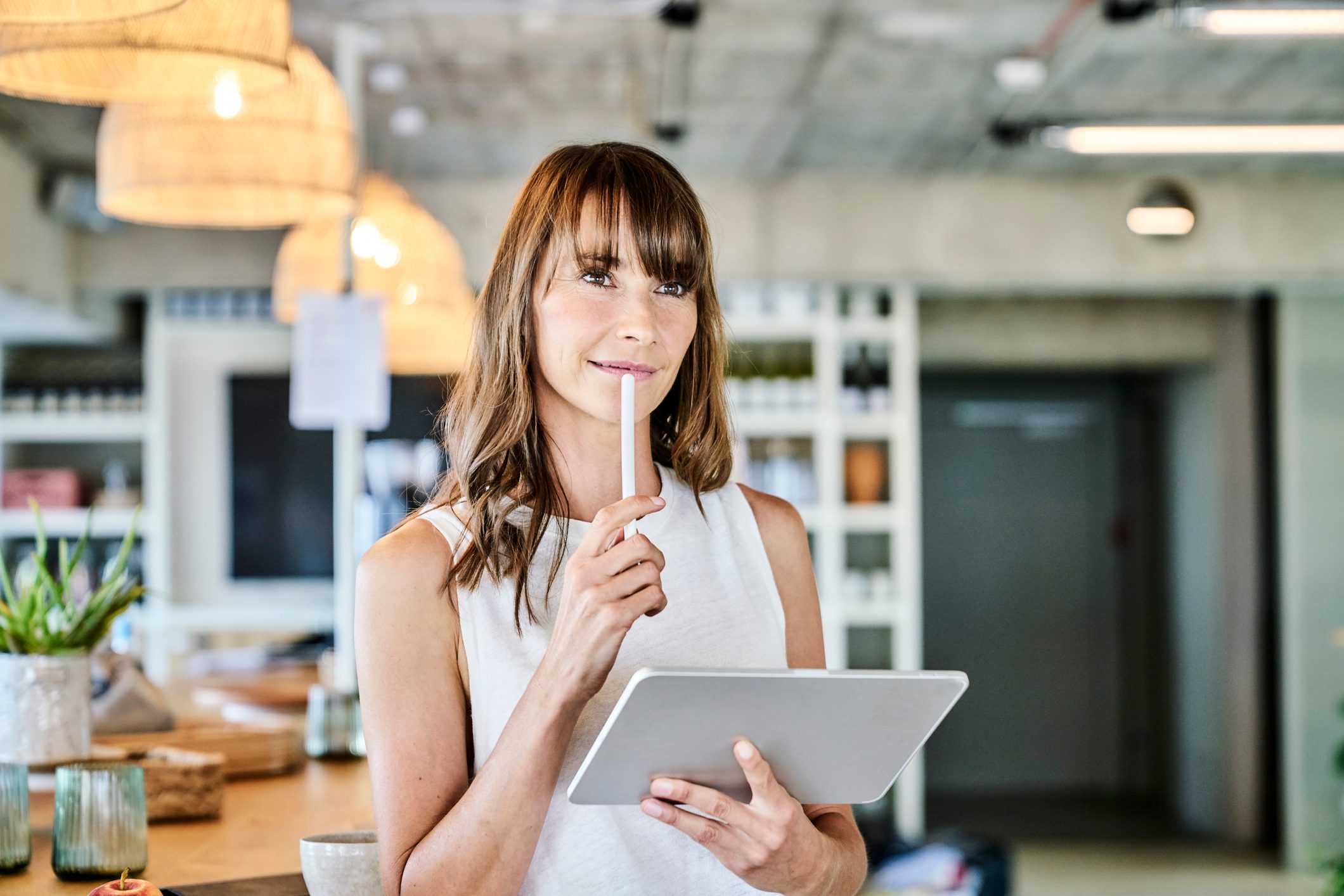 Thoughtful woman holding digitized pen and digital tablet while standing art home