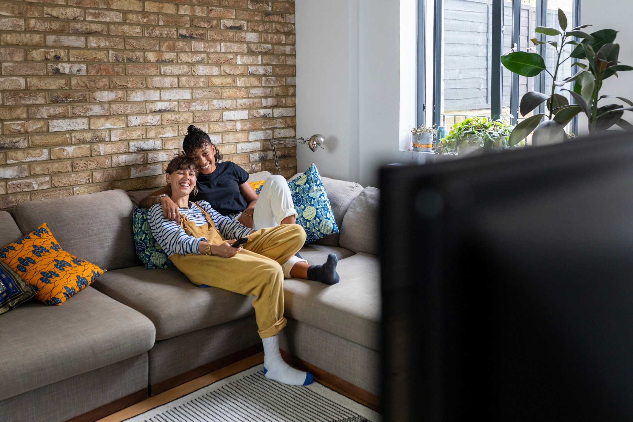 Smiling lesbian couple watching television while sitting on sofa at home