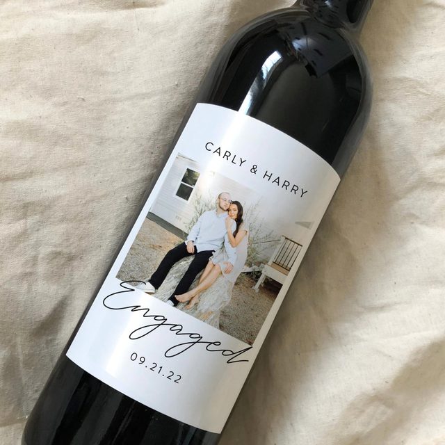 A wine bottle displays an engagement photo and text reading 