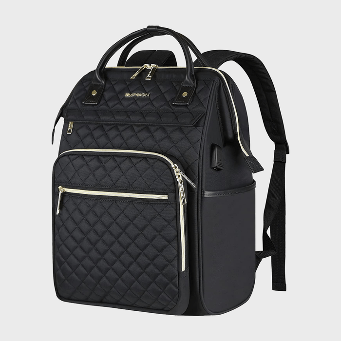 Black quilted backpack stands, displaying multiple zippered pockets and adjustable straps, set against a plain gray backdrop.