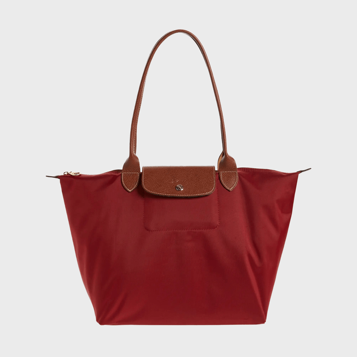Red tote bag with brown leather handles and flap, resting against a plain white background.