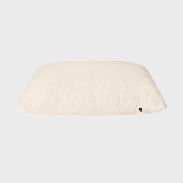 A beige pillow rests on a plain, light gray background, featuring a small green tag on its side.