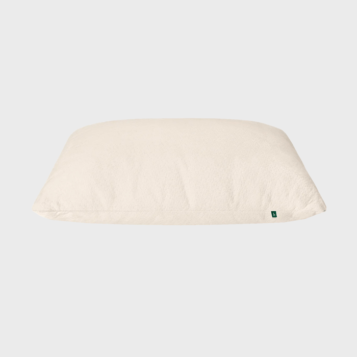 A beige pillow rests on a plain, light gray background, featuring a small green tag on its side.
