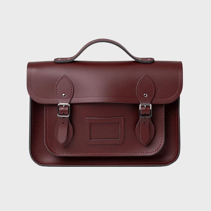 A brown leather satchel with buckle straps rests against a plain background, featuring a handle and stitched detailing.