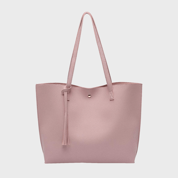 A pink textured tote bag hangs with long straps and a tassel, set against a plain white background.