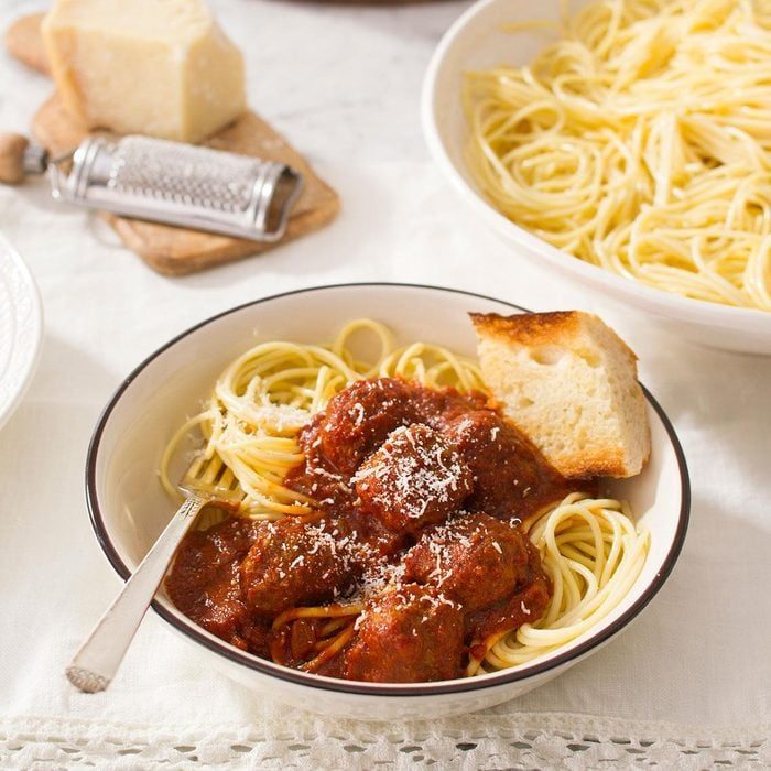 Spaghetti topped with meatballs and sauce, garnished with grated cheese and bread, is served in a bowl on a white tablecloth.