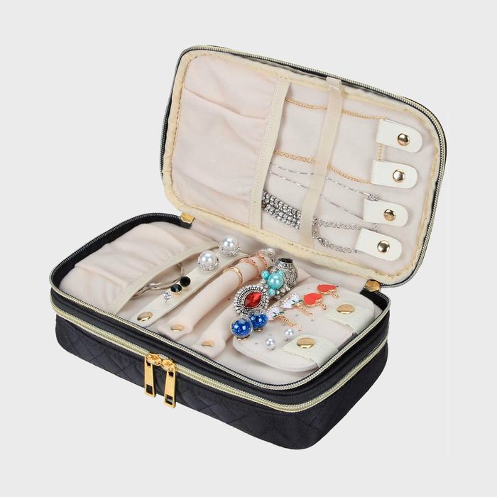 Jewelry case holding rings and necklaces, organized neatly, with a soft beige interior and black exterior, lying open on a plain background.