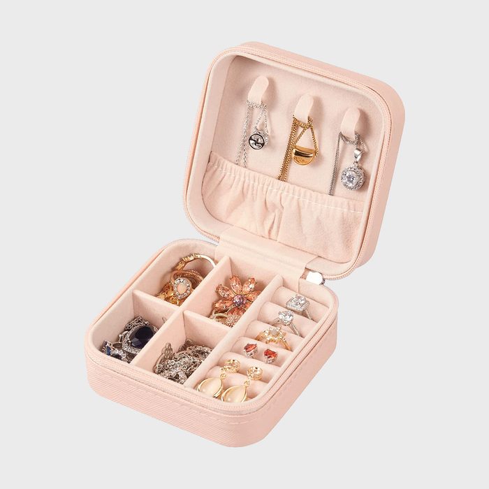 Jewelry box open, displaying rings, earrings, and necklaces, inside a soft, beige compartmentalized interior against a plain background.