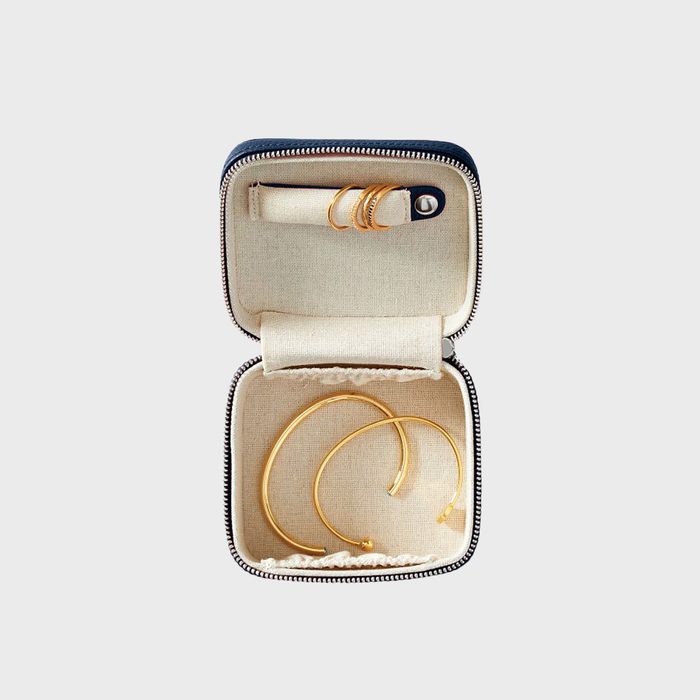 Jewelry box contains gold rings and bracelets, resting inside a lined, open case with a black zipper, displayed on a plain background.
