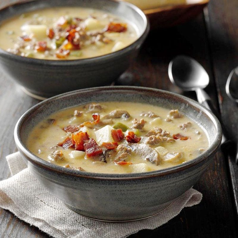 Bowl holds creamy soup with bacon and vegetables; placed on a cloth, accompanied by a spoon on a wooden table.