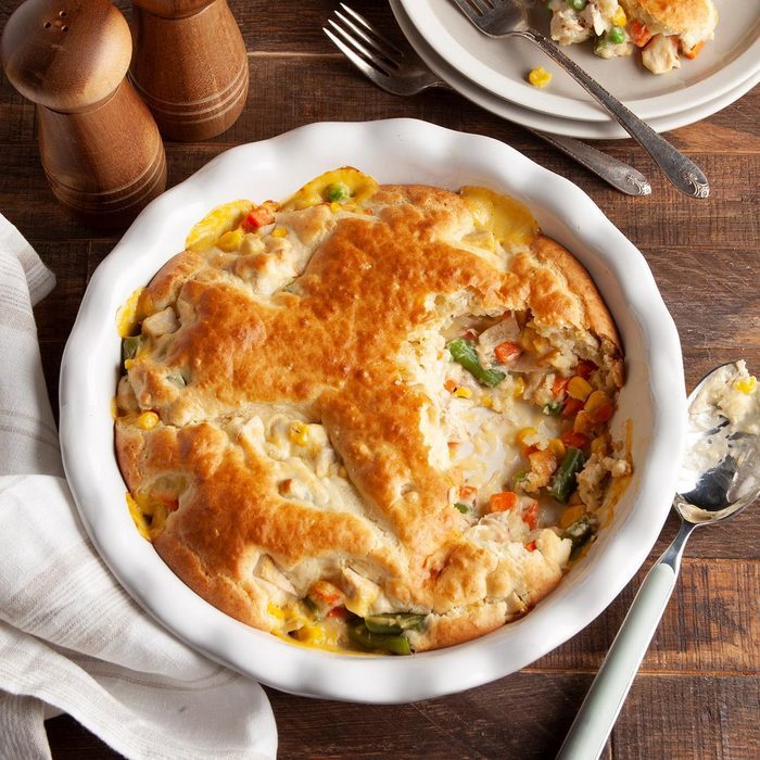 Golden-brown pot pie sits partially eaten in a white dish, surrounded by a spoon, fork, knife, salt, pepper shakers, and a cloth napkin.