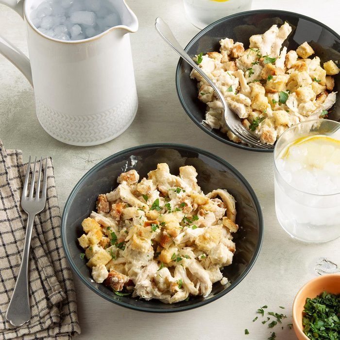 Bowls contain creamy chicken and croutons; garnished with parsley. A pitcher of ice water, drinking glass, fork, and napkin sit nearby on a table.