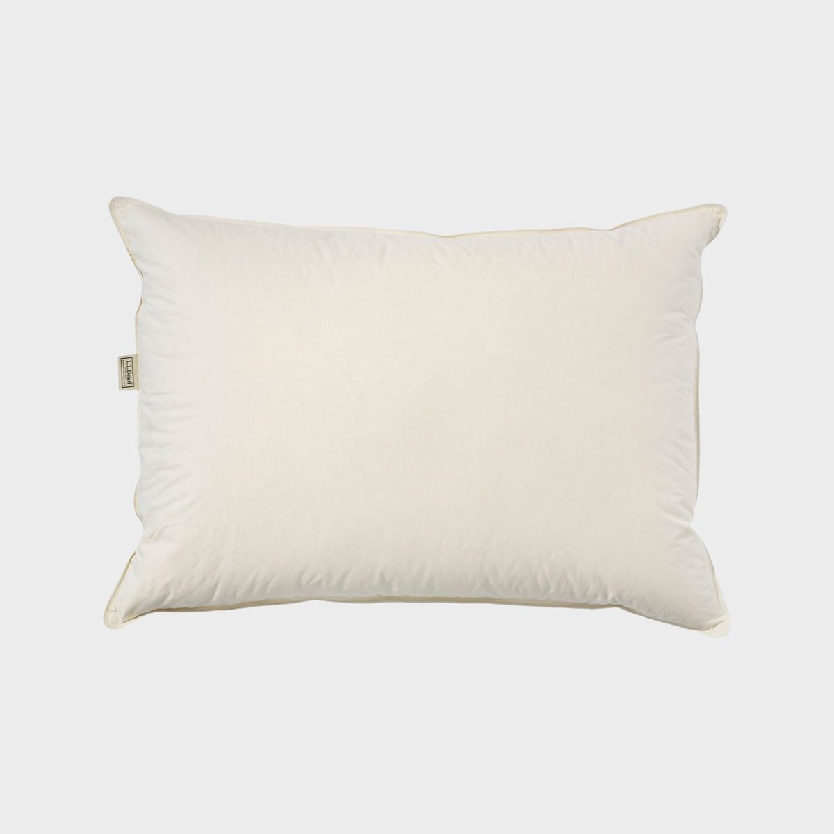 A rectangular white pillow lies flat against a plain light gray background, displaying a small fabric label on its side.