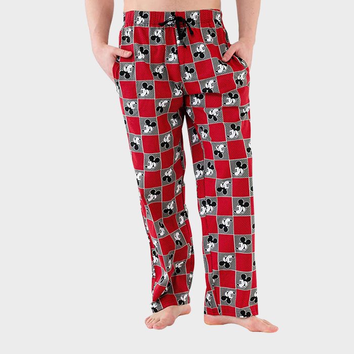 Pajama pants patterned with red and black checkered squares, featuring cartoon faces, are worn by a person standing barefoot in a plain setting.