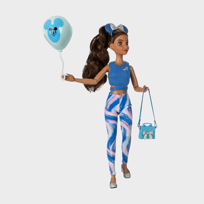 Doll holding balloon and purse, wearing blue top and swirl-patterned leggings in a plain setting.