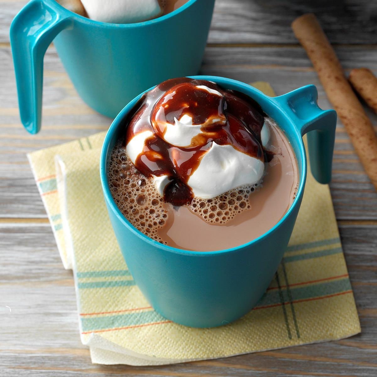 Mug filled with hot chocolate topped with whipped cream and chocolate syrup, resting on a napkin on a wooden table.