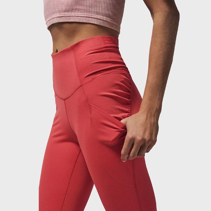 Person wearing red leggings, adjusting waist, in a studio setting.