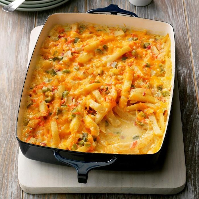 A cheesy baked casserole, featuring melted cheese and colorful vegetables, sits in a black rectangular dish on a wooden table.