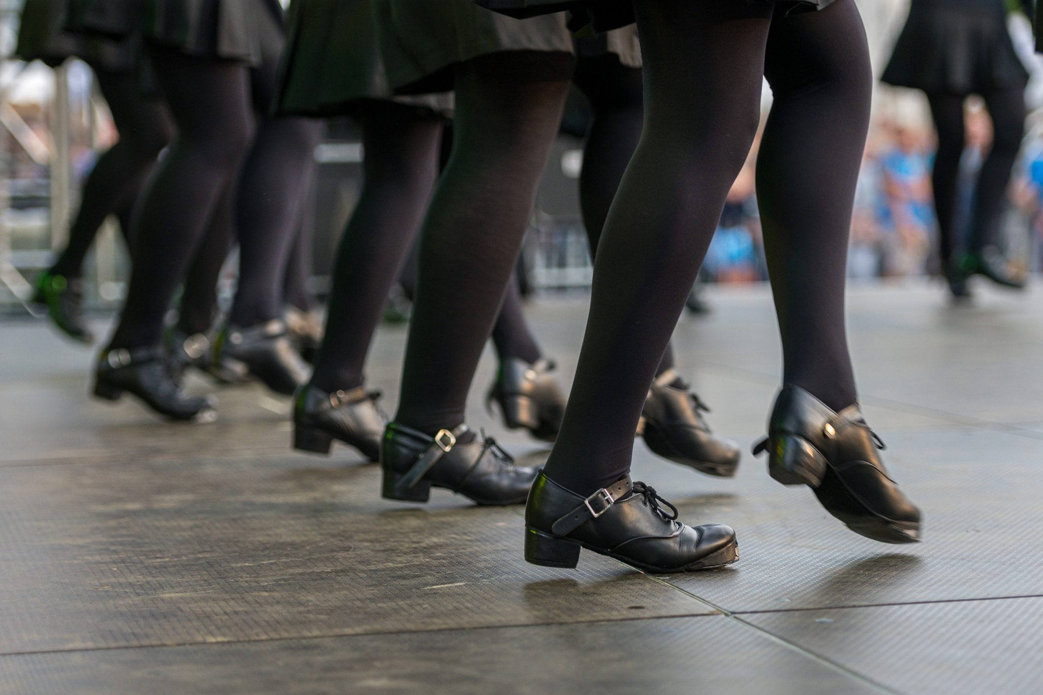 Tap shoes rhythmically dance on a stage, surrounded by an audience in soft focus, capturing a dynamic performance scene.