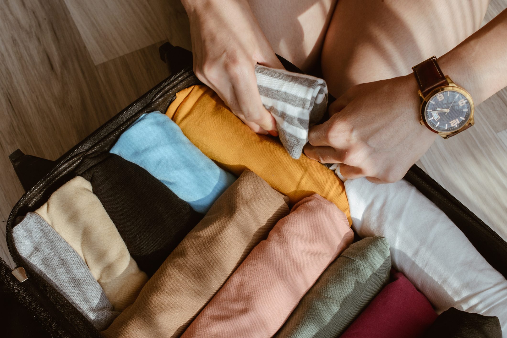 Close up of tourist woman open suitcase roll and pack colorful cloths for travelling.