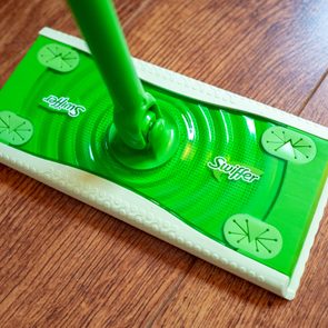 A green Swiffer mop rests on a wooden floor, displaying the brand name on its surface.