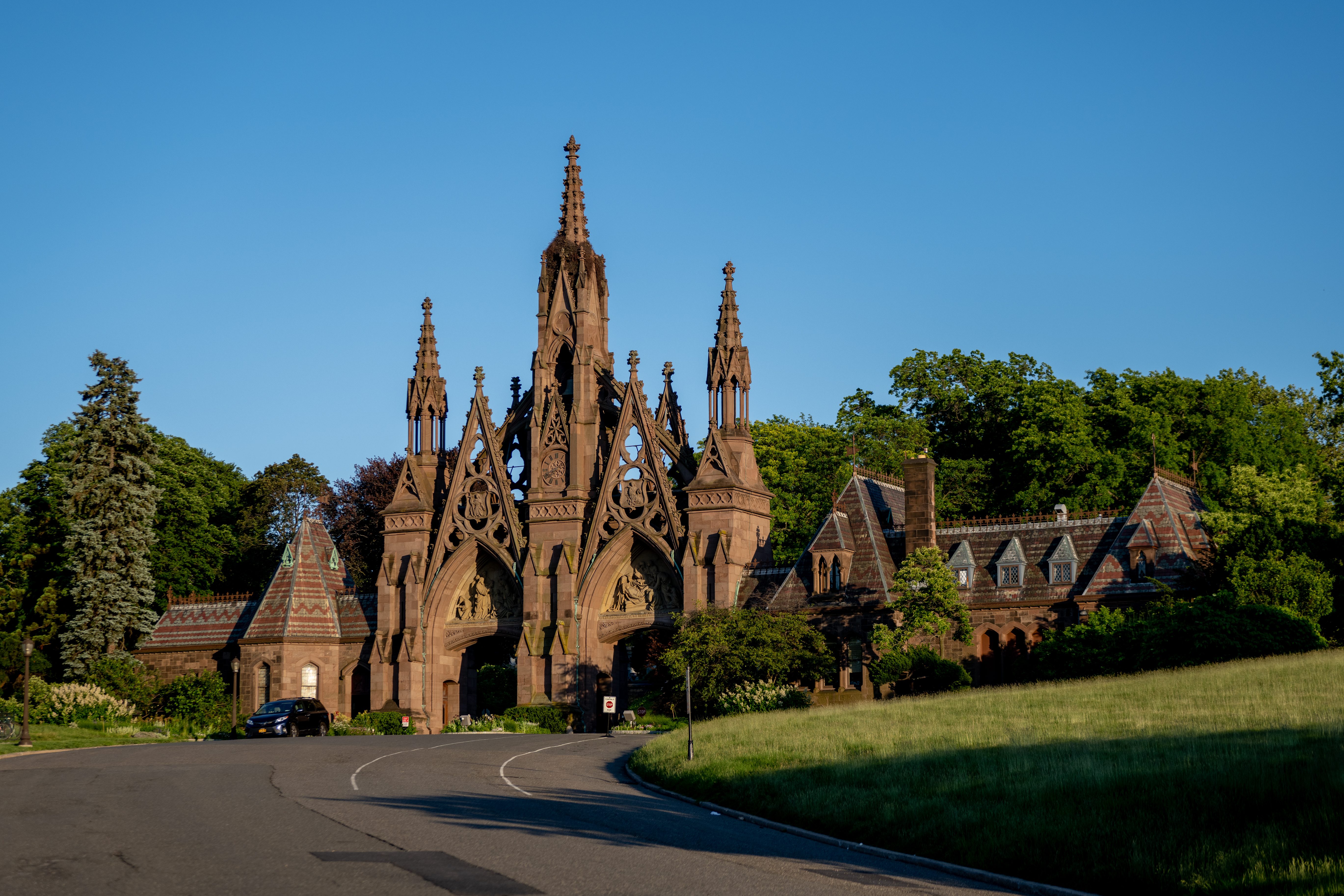 Gothic archway towers above a roadway, surrounded by lush greenery and trees under a clear blue sky.