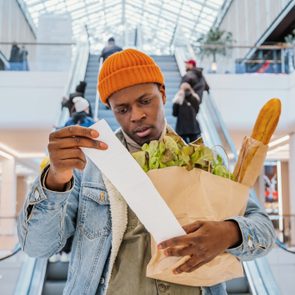 Person examines receipt while holding groceries in an indoor shopping mall near escalators.